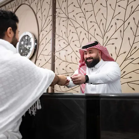 Swissotel Makkah Mecca Exterior photo The image shows two individuals engaged in a handshake. One person, dressed in white traditional attire, appears to be greeting the other, who is wearing a thobe and a traditional headscarf (ghutrah). The background features decorative wall art and a